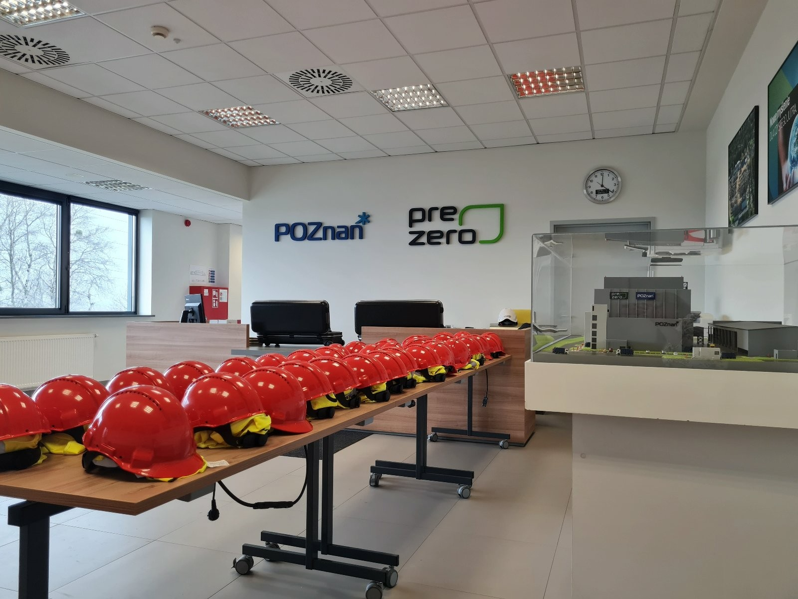 Na zdjęciu widać ułożone na stołach czerwone kaski ochronne. Po prawej stronie w szklanej gablocie jest makieta spalani. Na ścianie na wprost widnieje logo Poznania i firmy PreZero