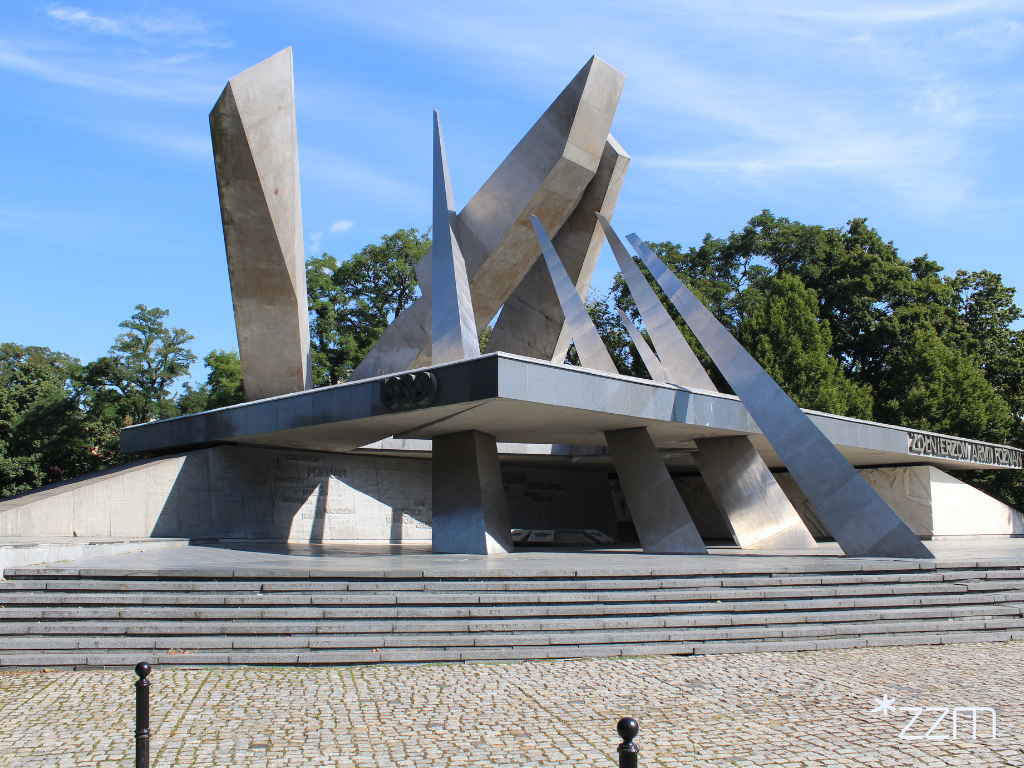 Pomnik Armii "Poznań" widziany od strony szerokich schodów. Monument tworzą wysokie, ostro zakończone elementy ustawione pod różnymi kątami oraz pozioma konstrukcja z napisem "Żołnierzom Armii Poznań".