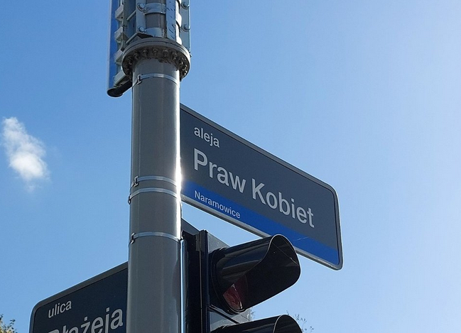 tabliczka z nazwą ulicy Aleja Praw Kobiet zainstalowana na słupie