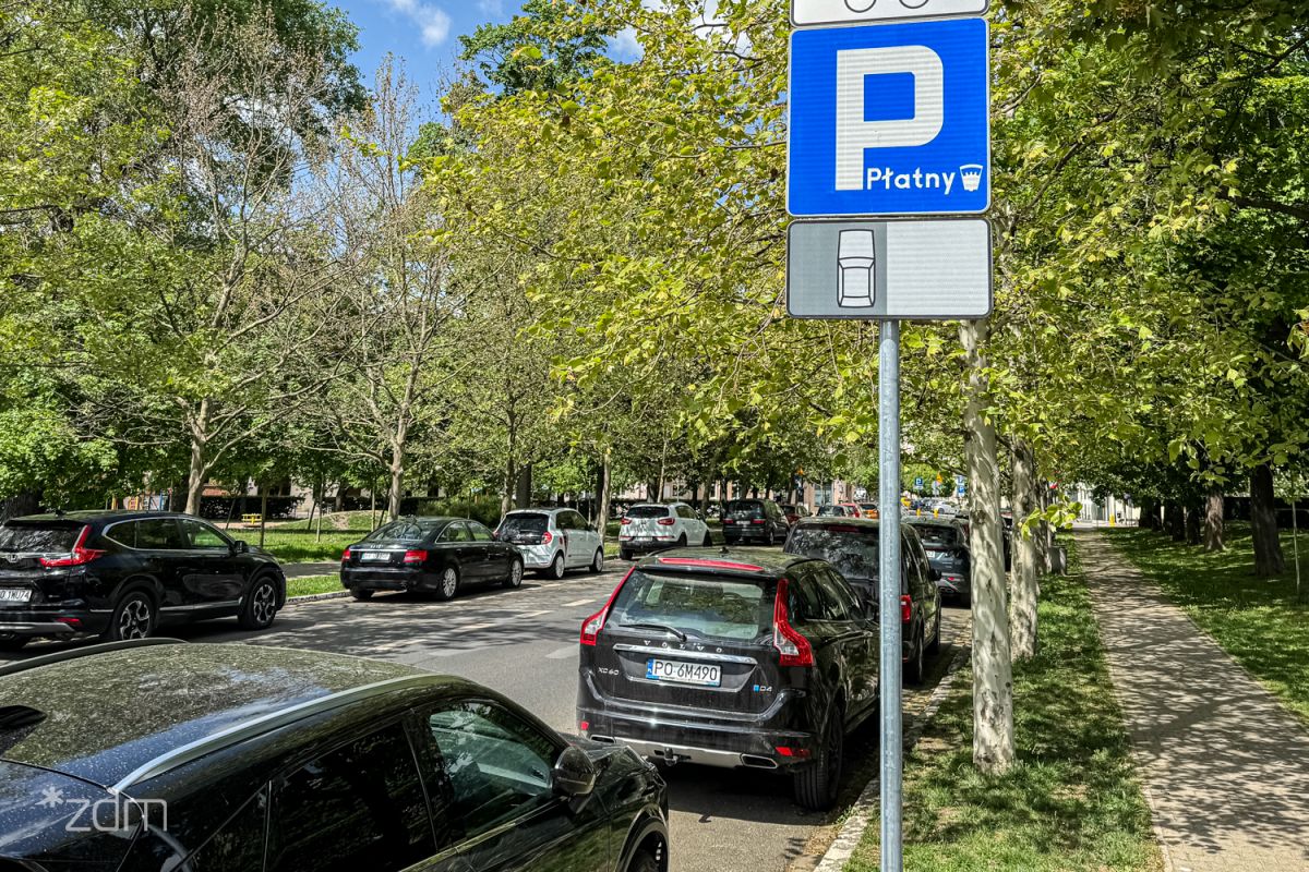 Ulica z parkującymi samochodami i znakiem informującym o płatnym parkowaniu