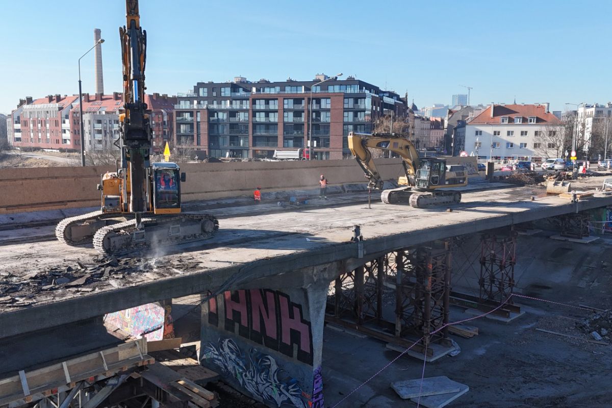 Widok na prace budowlane trwające na moście. Widać cieżki sprzęt budowlany i maszyny.