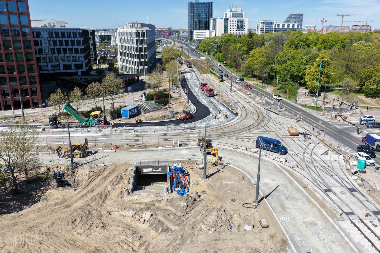 Widok z lotu ptaka na duże skrzyżowanie ulic na którym trwa remont. Widać samochody cięzarowe i maszyny budowlane. W tle wysokie budynki.